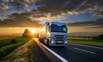 Truck driving on the asphalt road in rural landscape at sunset with dark clouds